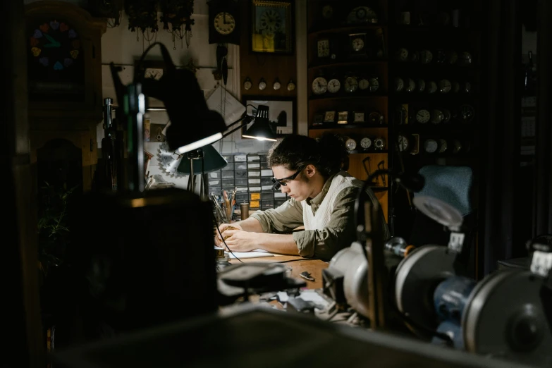 a man sitting at a desk writing on a piece of paper, by Matthias Stom, pexels contest winner, arbeitsrat für kunst, intricate electronics, industrial lighting, in a workshop, avatar image