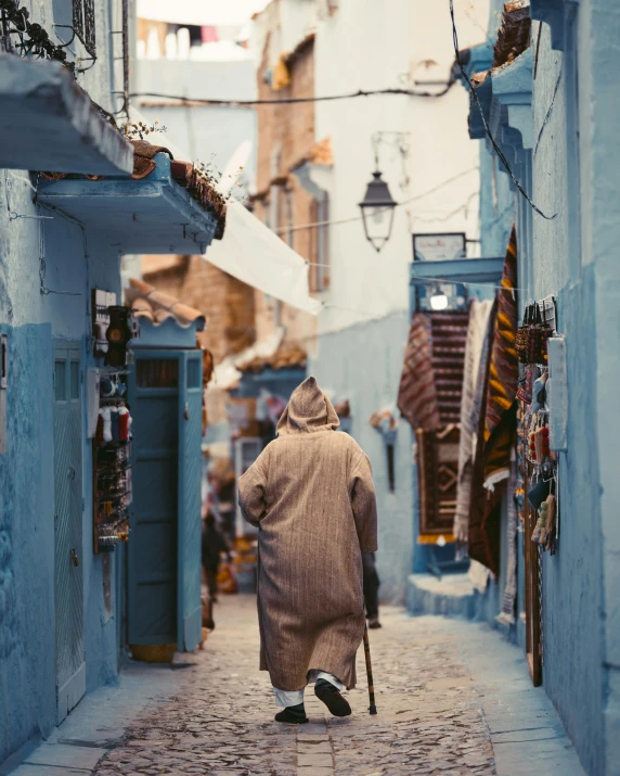 an old man walking down a narrow street, by Julia Pishtar, trending on unsplash, blue robe, lgbtq, moroccan, in the winter