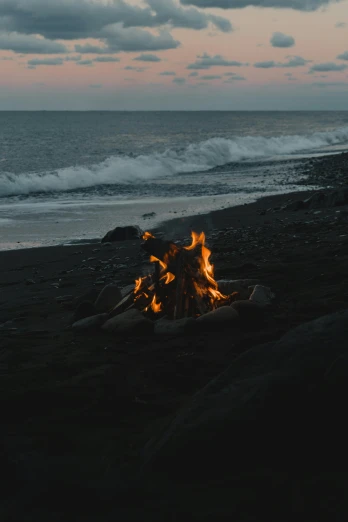 a campfire sitting on top of a beach next to the ocean, profile image, black sand, torrent, ignant