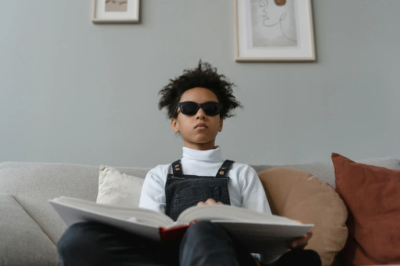 a woman sitting on a couch reading a book, by Adam Marczyński, pexels contest winner, black teenage boy, wearing shades, boy with neutral face, looking upwards