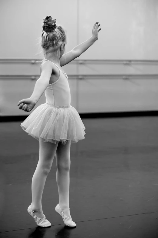 a black and white photo of a little girl in a tutu, arabesque, raised hand, looking across the shoulder, taken in 2 0 2 0, may)