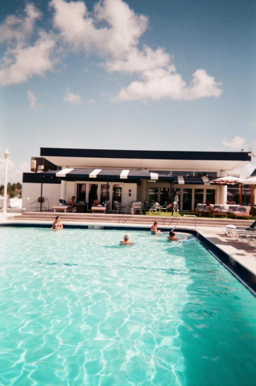 a group of people swimming in a large pool, ektachrome color photograph, bahamas, googie architecture, 1999 photograph