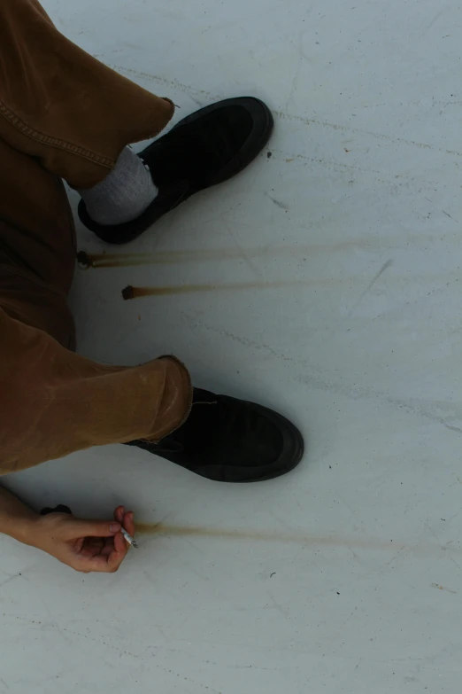 a person sitting on top of a snow covered ground, inspired by Andy Goldsworthy, with a straw, standing on a skateboard, marking lines, close up shot from the top