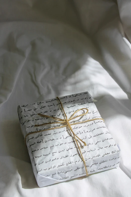 a wrapped gift sitting on top of a bed, by Alice Mason, pexels contest winner, hurufiyya, arabic calligraphy, wearing white pajamas, packaging, multiple stories