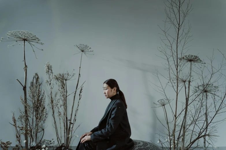 a woman sitting on a rock surrounded by plants, inspired by Fei Danxu, unsplash, conceptual art, a man wearing a black jacket, on a pale background, portrait mode photo, 千 葉 雄 大