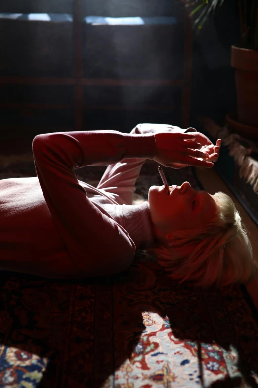 a woman laying on a rug in a room, inspired by Elsa Bleda, trending on pexels, ray of light through white hair, dramatic smoking pose, androgynous person, red and cinematic lighting