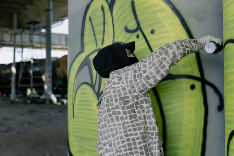 a person standing in front of a graffiti covered wall, graffiti, cloak covering face, islamic, filling the frame, grey
