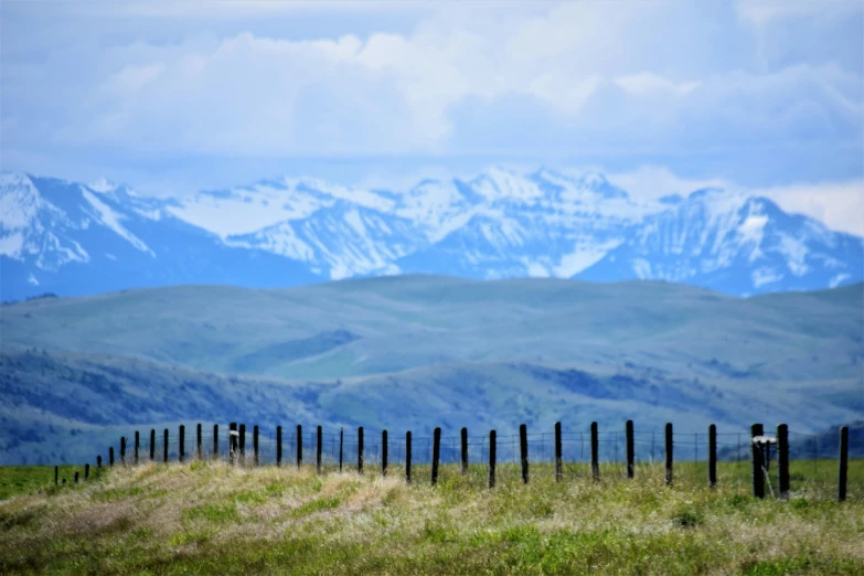 a fence in a field with mountains in the background, by Brigette Barrager, pexels contest winner, montana, background image, bakelite rocky mountains, seen from the long distance