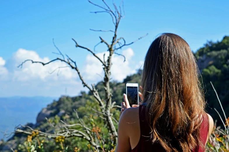 a woman taking a picture with her cell phone, a picture, by Niko Henrichon, pexels contest winner, monserrat gudiol, nature outside, blue sky, back