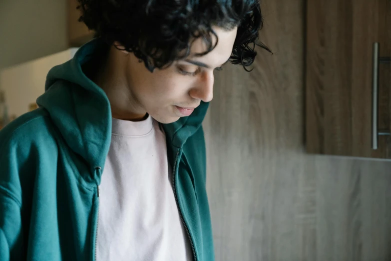 a young man using a cell phone in a kitchen, by Caro Niederer, trending on pexels, renaissance, wearing green jacket, young middle eastern woman, shy looking down, curly and short top hair