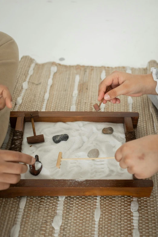 a group of people sitting on top of a rug, on a wooden tray, rock and sand around, samurai duel, tiny sticks