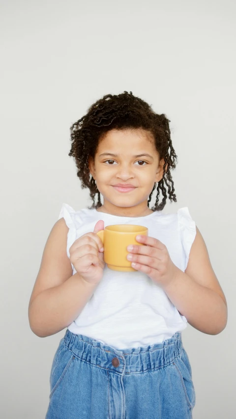 a little girl holding a cup of coffee, light brown skin, press shot, square, yellow hue