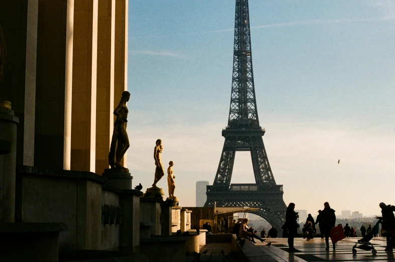 a group of people standing in front of the eiffel tower, statues, afternoon light, tall structures, during the day