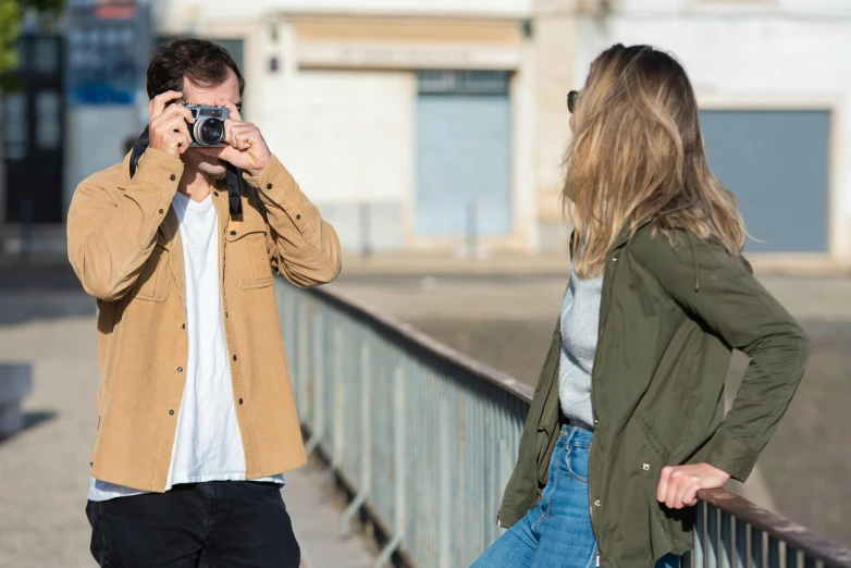 a man taking a picture of a woman with a camera, by Nina Hamnett, trending on unsplash, photorealism, an aviator jacket and jorts, photoshoot for skincare brand, outlive streetwear collection, action shot girl in parka