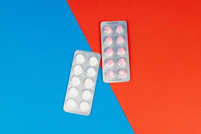 a couple of pills sitting on top of a red and blue background, inspired by Damien Hirst, pexels, antipodeans, pair of keycards on table, pink white turquoise, sleek round shapes, white plastic