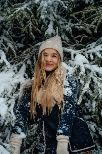 a woman standing in front of a tree covered in snow, with long blond hair, beanie, vacation photo, trending photo