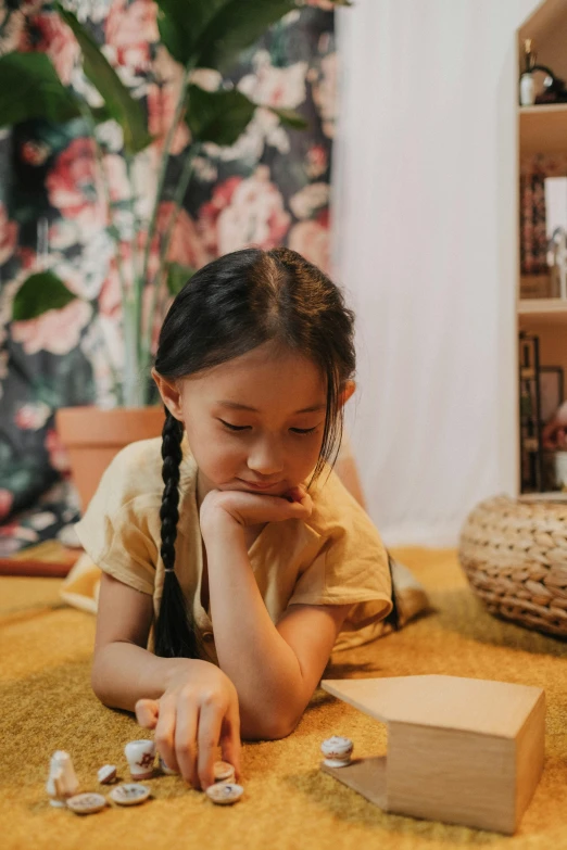 a little girl laying on the floor playing with coins, a child's drawing, by artist, pexels contest winner, village girl reading a book, long chin, gif, young asian girl