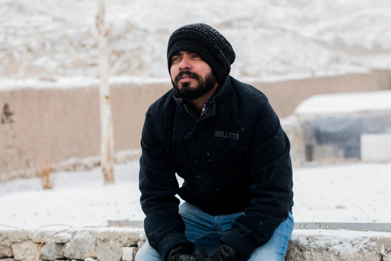 a man sitting on a stone wall in the snow, a portrait, inspired by Abdullah Gërguri, pexels contest winner, hurufiyya, a portrait of rahul kohli, still from the movie, skilled homeless, profile pic