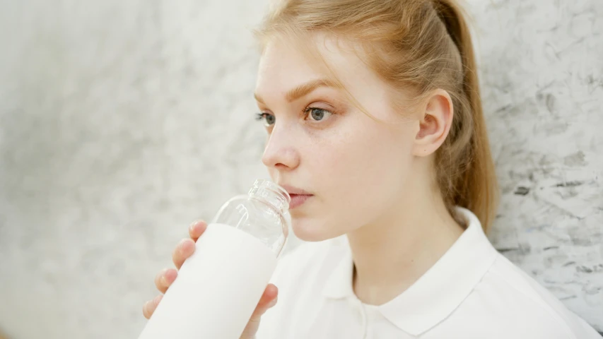 a young woman drinking a glass of milk, by Ellen Gallagher, trending on pexels, pale thin lips, teenage female schoolgirl, holding a bottle of arak, close up face