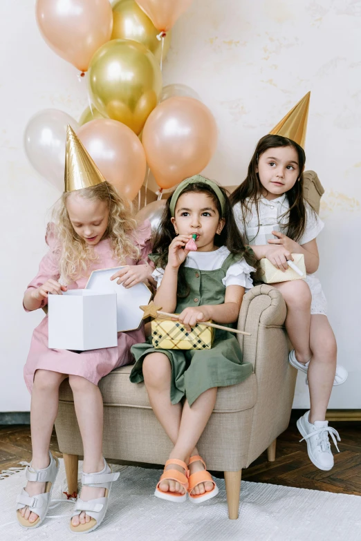 a group of young girls sitting on top of a couch, by Nicolette Macnamara, pexels, renaissance, party hats, holding a gold bag, holding a balloon, linen