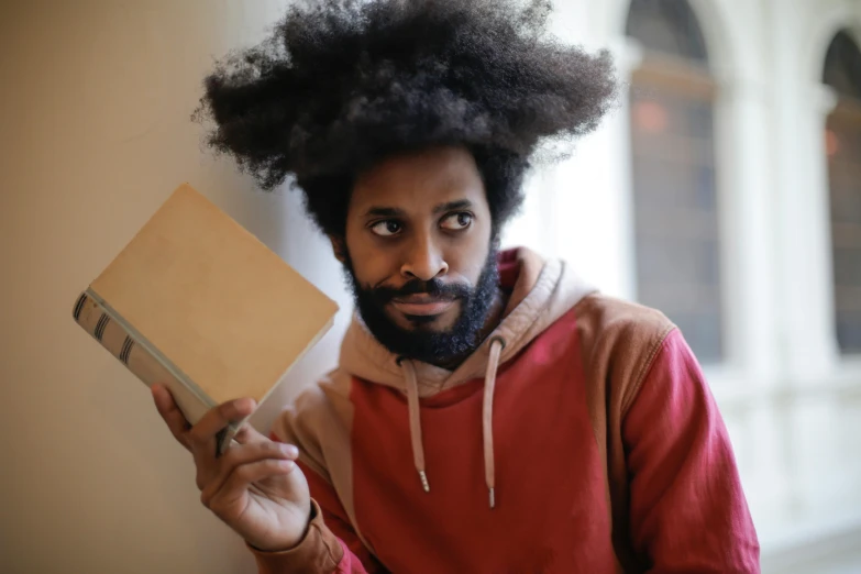 a man with a beard holding a book, a portrait, pexels contest winner, afro hair, looking threatening, instagram post, playful smirk