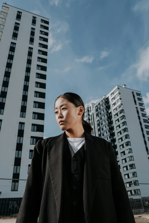 a man standing in front of a tall building, an album cover, inspired by Cheng Jiasui, pexels contest winner, portrait androgynous girl, woman in black robes, (((luke chueh))), concentrated buildings