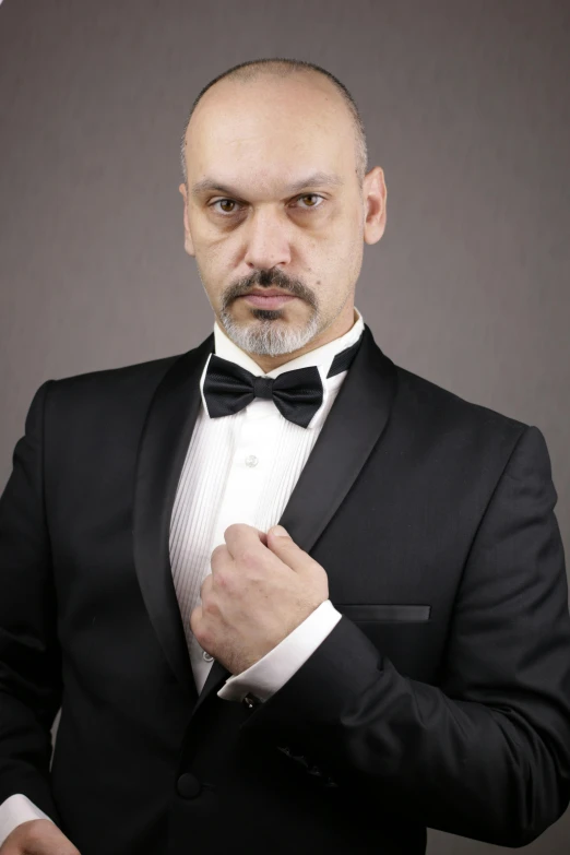 a man in a tuxedo adjusting his bow tie, an album cover, inspired by Edi Rama, posing ready for a fight, headshot photograph, metabaron, in a fighting stance