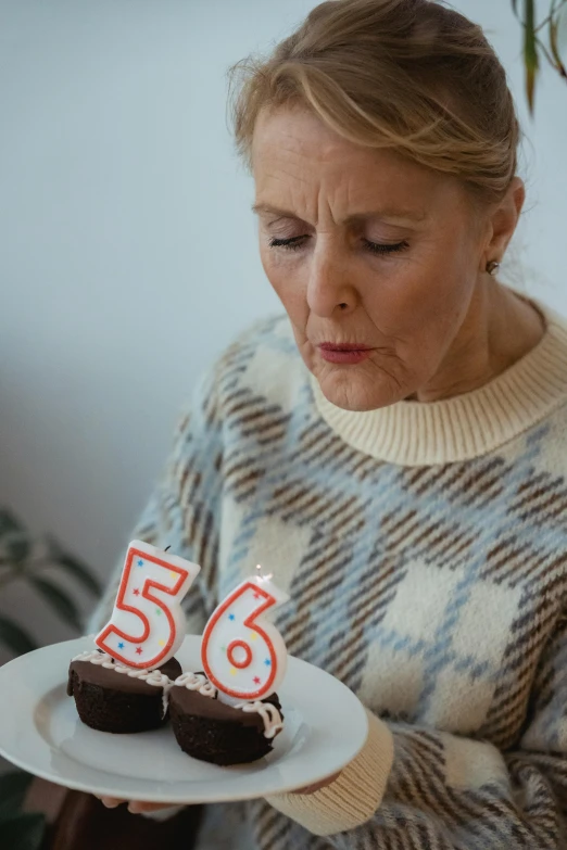 a woman holding a plate with two cupcakes on it, by Adam Marczyński, pexels contest winner, looking old, he is about 50 years old, gif, dripping candles