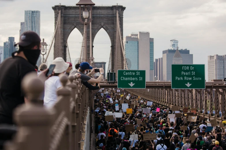 a crowd of people standing on top of a bridge, placards, watching new york, photography: journalism, fan favorite