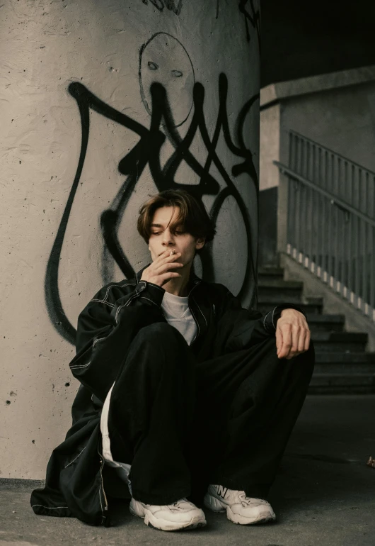 a man sitting on the ground smoking a cigarette, an album cover, pexels contest winner, realism, androgynous person, profile pic, black graffiti, thick jawline