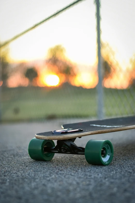 a skateboard sitting on the ground in front of a fence, during a sunset, profile image, a green, zoomed in