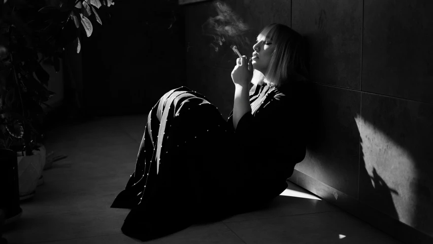 a woman sitting on the ground smoking a cigarette, a black and white photo, inspired by Leila Faithfull, wearing a black robe, profile image, alternate album cover, portrait a woman like reol