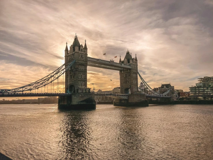a bridge over a body of water under a cloudy sky, an album cover, pexels contest winner, tower bridge, golden hour photograph, brown, a cozy