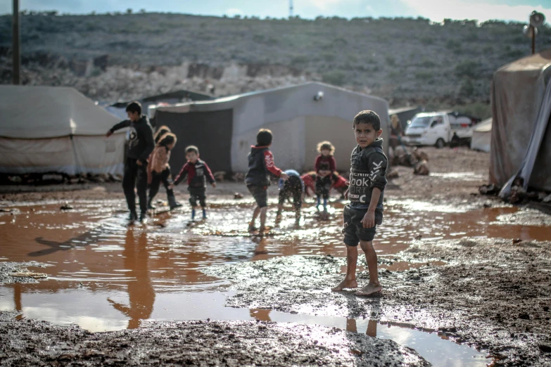 a group of children playing in a muddy field, by Daren Bader, trending on unsplash, hurufiyya, lebanon kirsten dunst, in a war - torn desert village, stands in a pool of water, “ iron bark