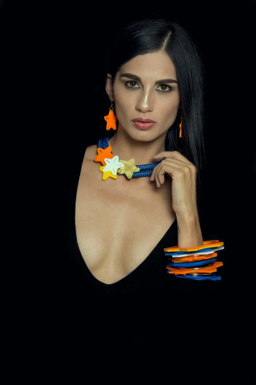 a woman posing in front of a black background, a colorized photo, by Robbie Trevino, conceptual art, bracelets and necklaces, coloured in blueberra and orange, made of silk paper, stars