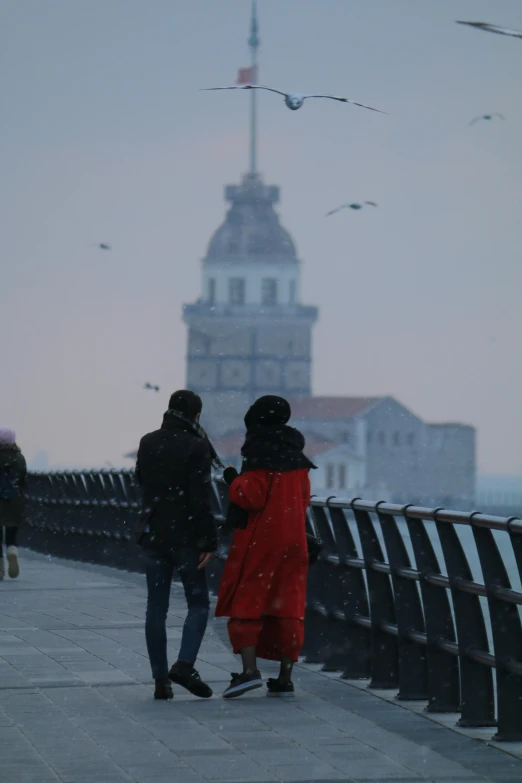 a group of people standing on top of a pier next to a body of water, by Nabil Kanso, during snowfall, big towers, low quality photo, istanbul