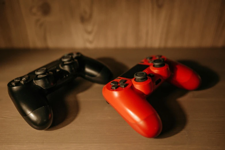 a couple of video game controllers sitting on top of a wooden table, red and black, shot on sony a 7, image, game