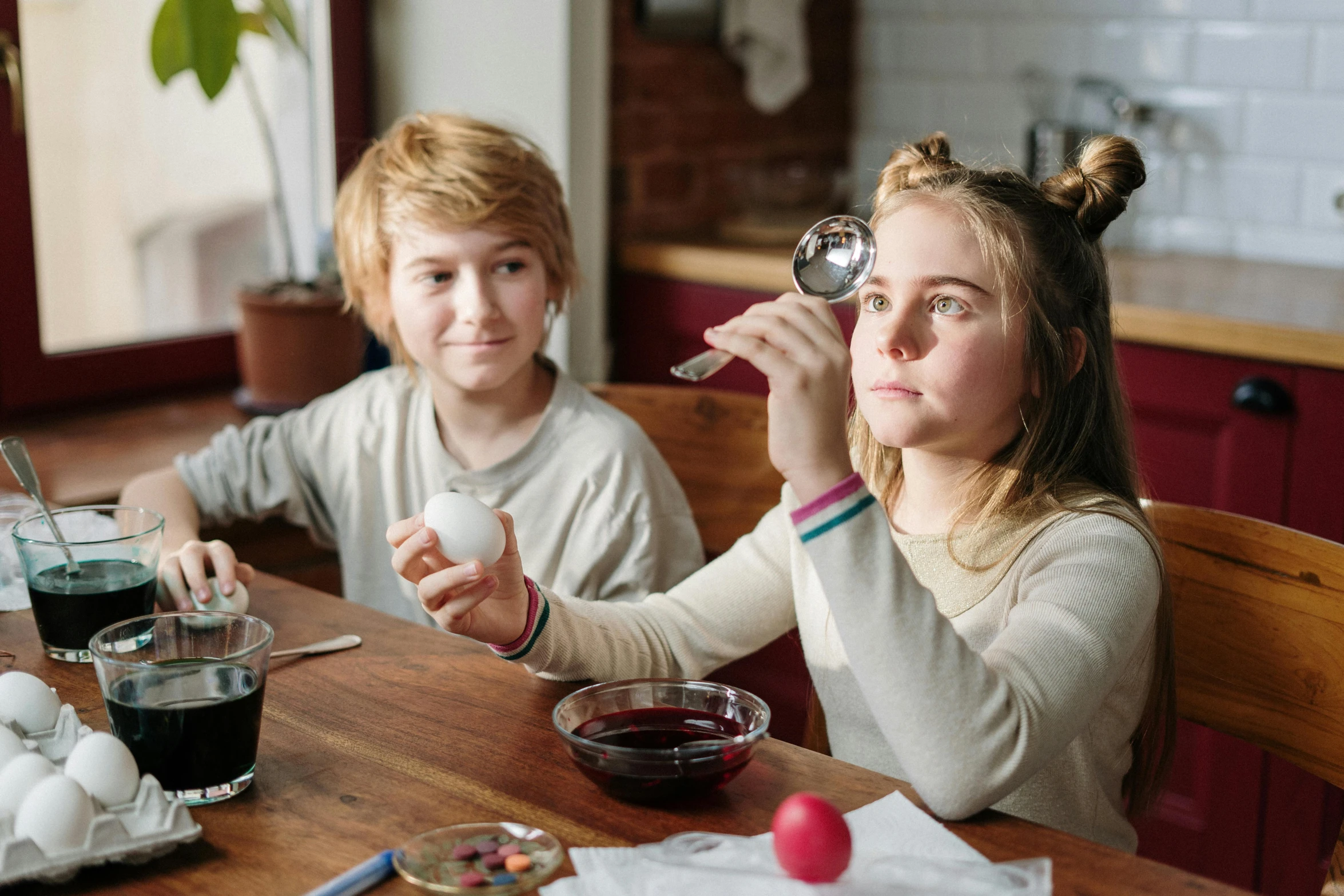 a couple of kids that are sitting at a table, pensive wizard examining eggs, scientific glassware, gen z, squashed berry stains