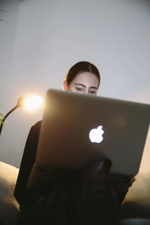 a woman sitting on a couch using a laptop computer, pexels, emerging from her lamp, with apple, low quality photo