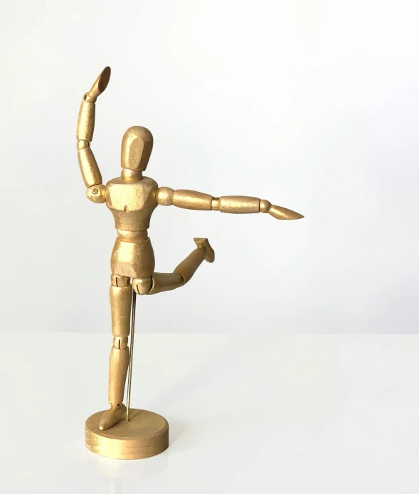 a gold figurine sitting on top of a white table, kinetic art, dynamic active running pose, wood art, kenner style action figure, ballet