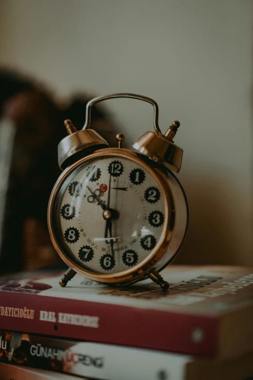 a clock sitting on top of a stack of books, dials, thumbnail, the golden hour, knickknacks