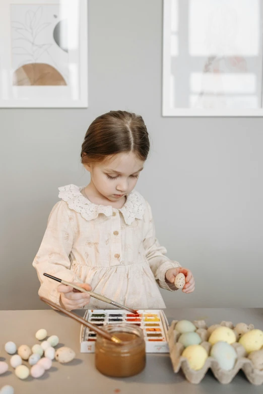 a little girl painting eggs on a table, inspired by Elsa Beskow, pexels contest winner, muted colors with minimalism, elegantly dressed, katelynn mini cute style, portrait of small