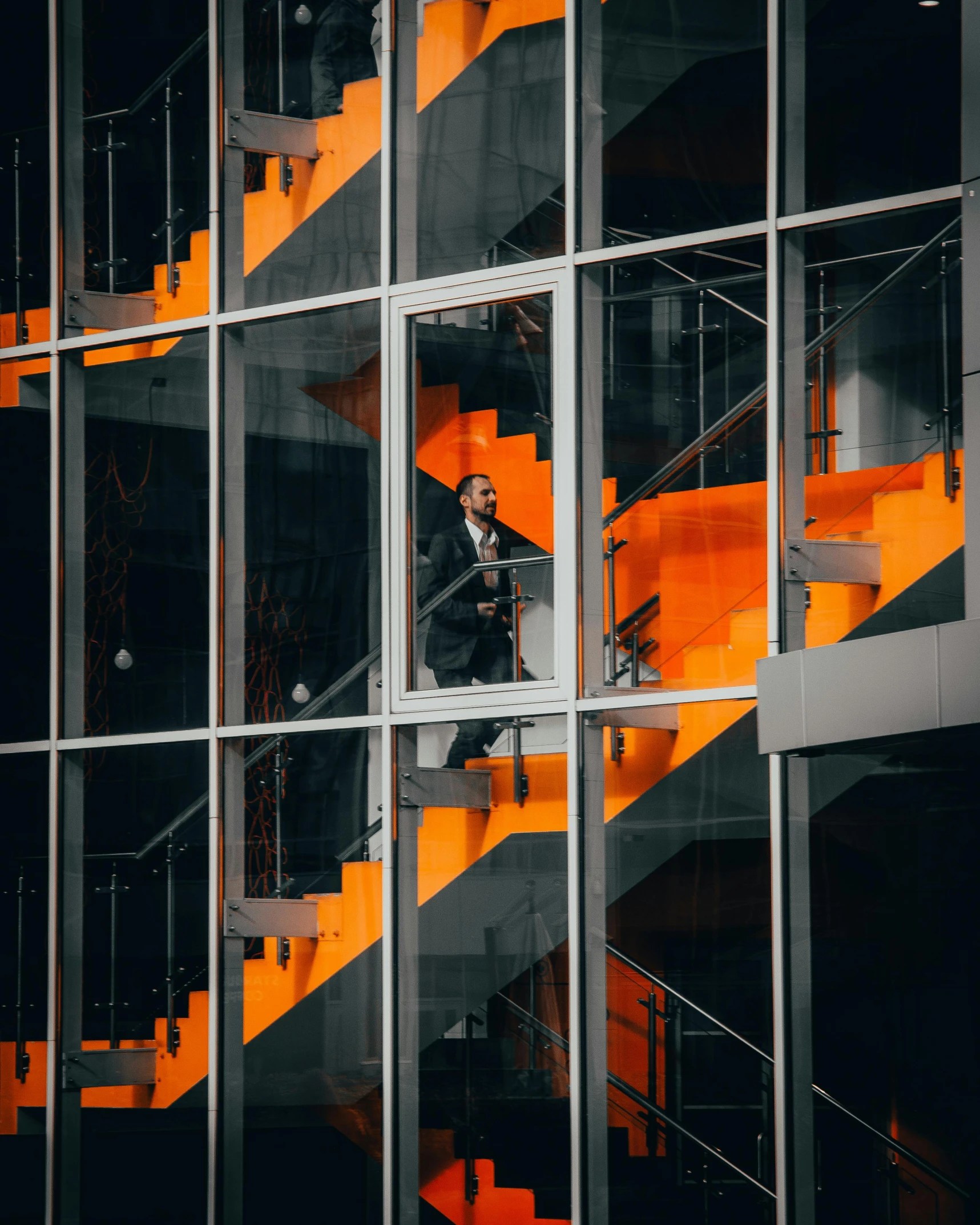 a man in a suit walking up a set of stairs, by Sebastian Spreng, pexels contest winner, modernism, orange and black, glass windows, standing on a ladder, thumbnail