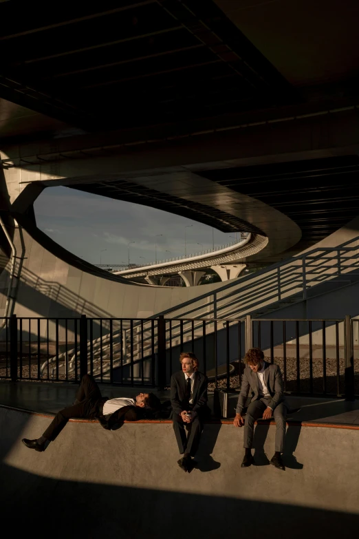 a group of people sitting on a bench under a bridge, an album cover, inspired by Zaha Hadid, unsplash, ignant, dapper, stadium, photographed for reuters