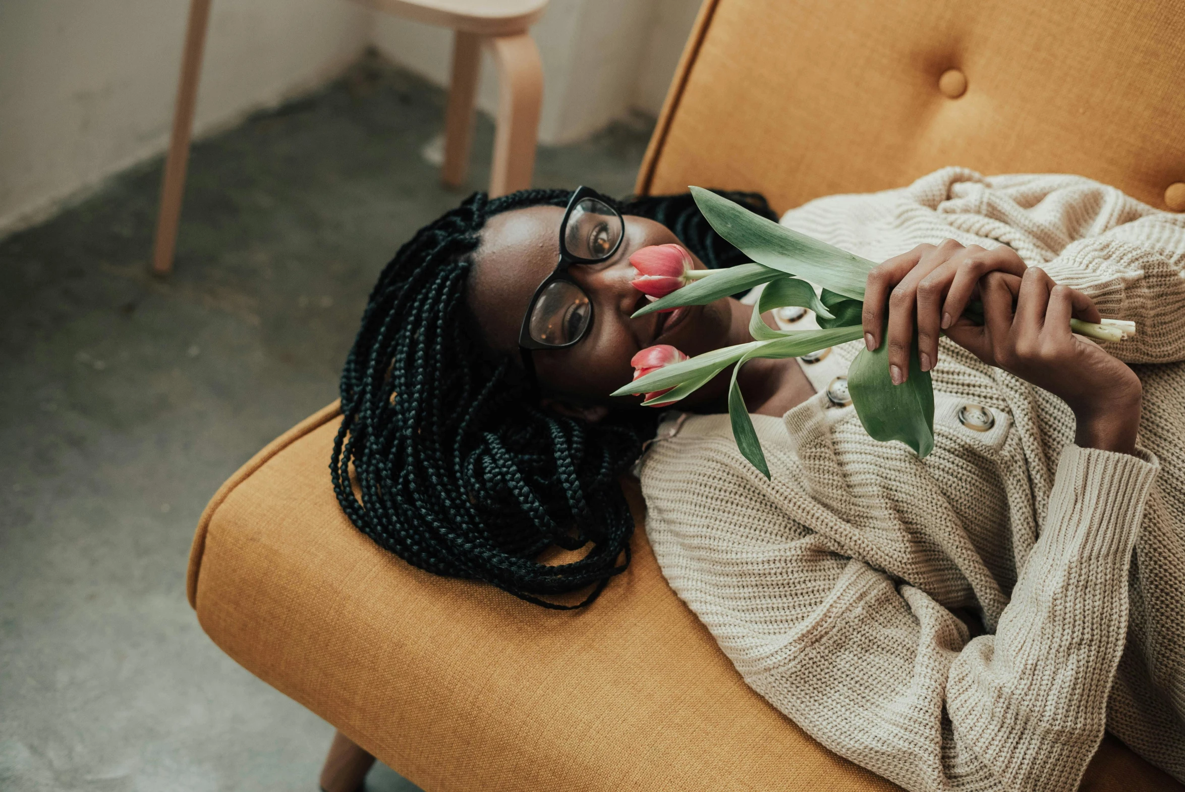 a woman laying on a couch with a flower in her mouth, pexels contest winner, nerdy black girl super hero, roses and tulips, hugging her knees, girl with glasses