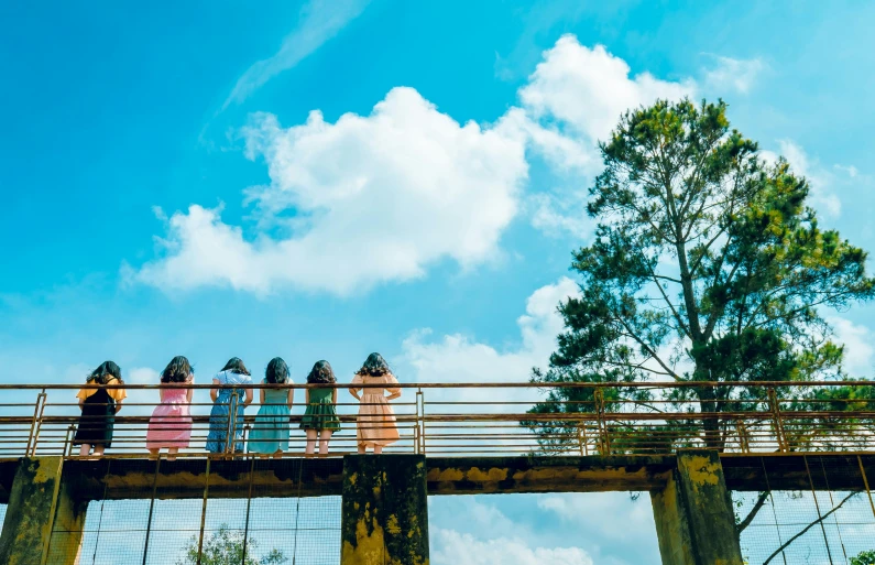 a group of people standing on top of a bridge, by Lucia Peka, pexels contest winner, ao dai, clear blue sky vintage style, girls resting, cotton candy trees