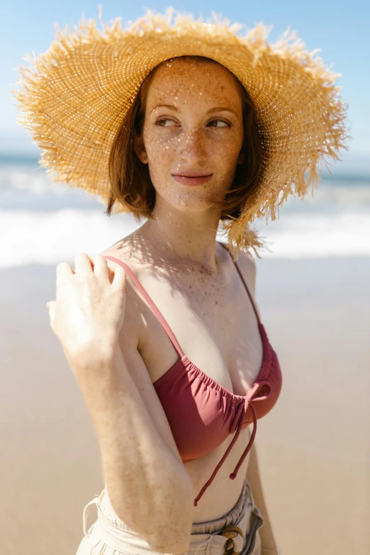 a woman wearing a straw hat on a beach, bralette, with pale skin, augmentation, manly