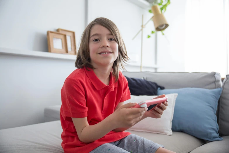 a little girl sitting on a couch playing a video game, pexels contest winner, happening, red shirt, he is holding a smartphone, while smiling for a photograph, aged 13