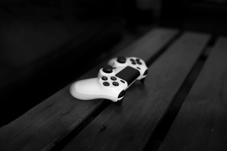 a video game controller sitting on top of a wooden table, a black and white photo, by Patrick Pietropoli, glossy white, playstation, white with black spots, game