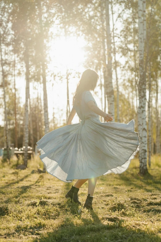 a woman in a white dress walking through a forest, by Eero Järnefelt, unsplash, dancing in the background, at sunrise in springtime, wide skirts, in sunny weather